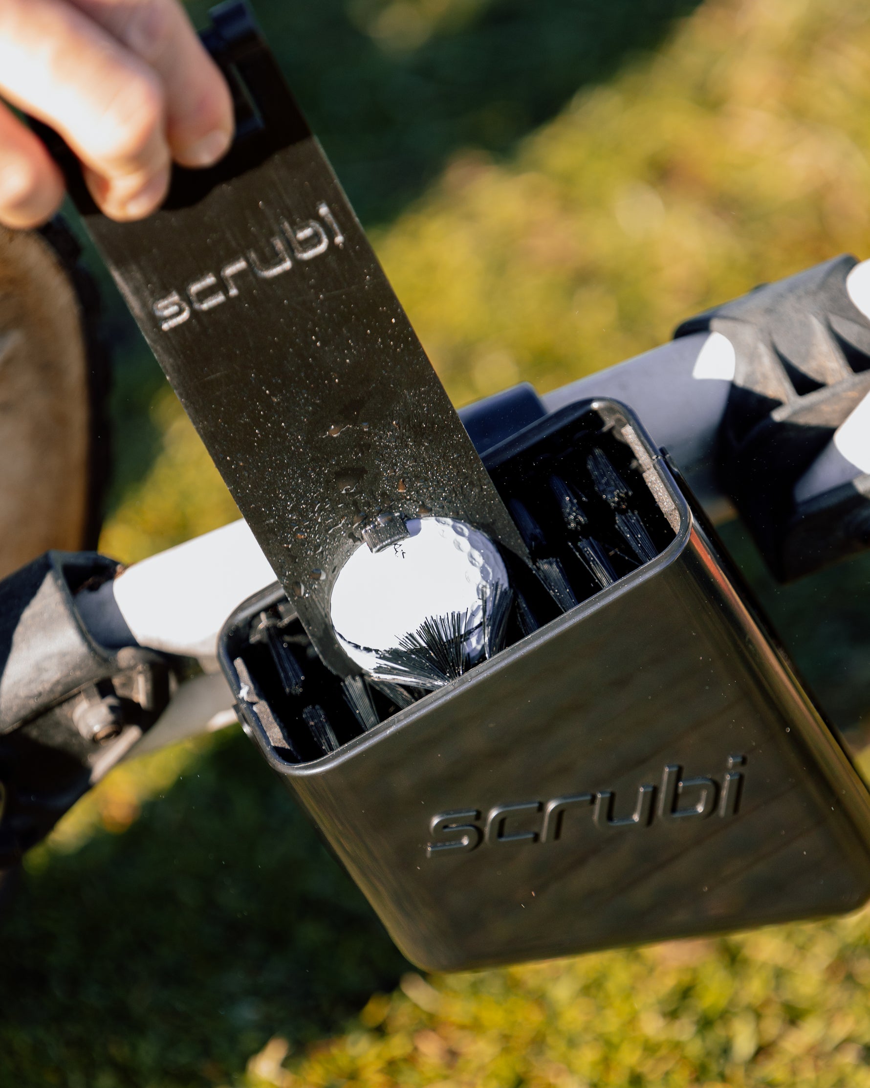 Scrubi golf club cleaner attached to a 3-wheel Clicgear, featuring durable bristles for effective club cleaning on the course with a golf ball cleaner cleaning a golf ball