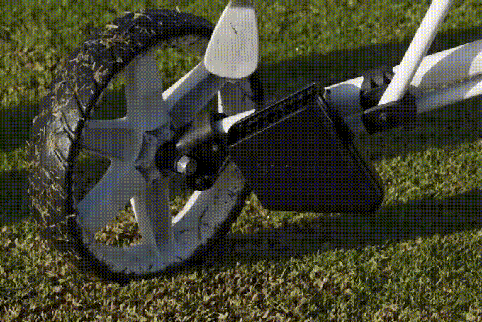 A Scrubi golf club cleaner, attached to a clicgear pushcart,  being used to clean a dirty golf club.