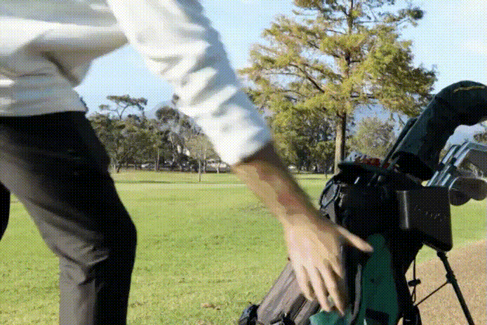 A golfer walking with his golf bag on his back with a Scrubi mounted to the bag, demonstrating no water spillage. 